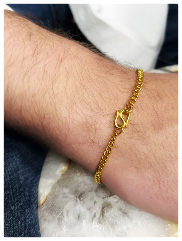 Gold chain bracelet with a distinctive clasp design, worn on a person's wrist.