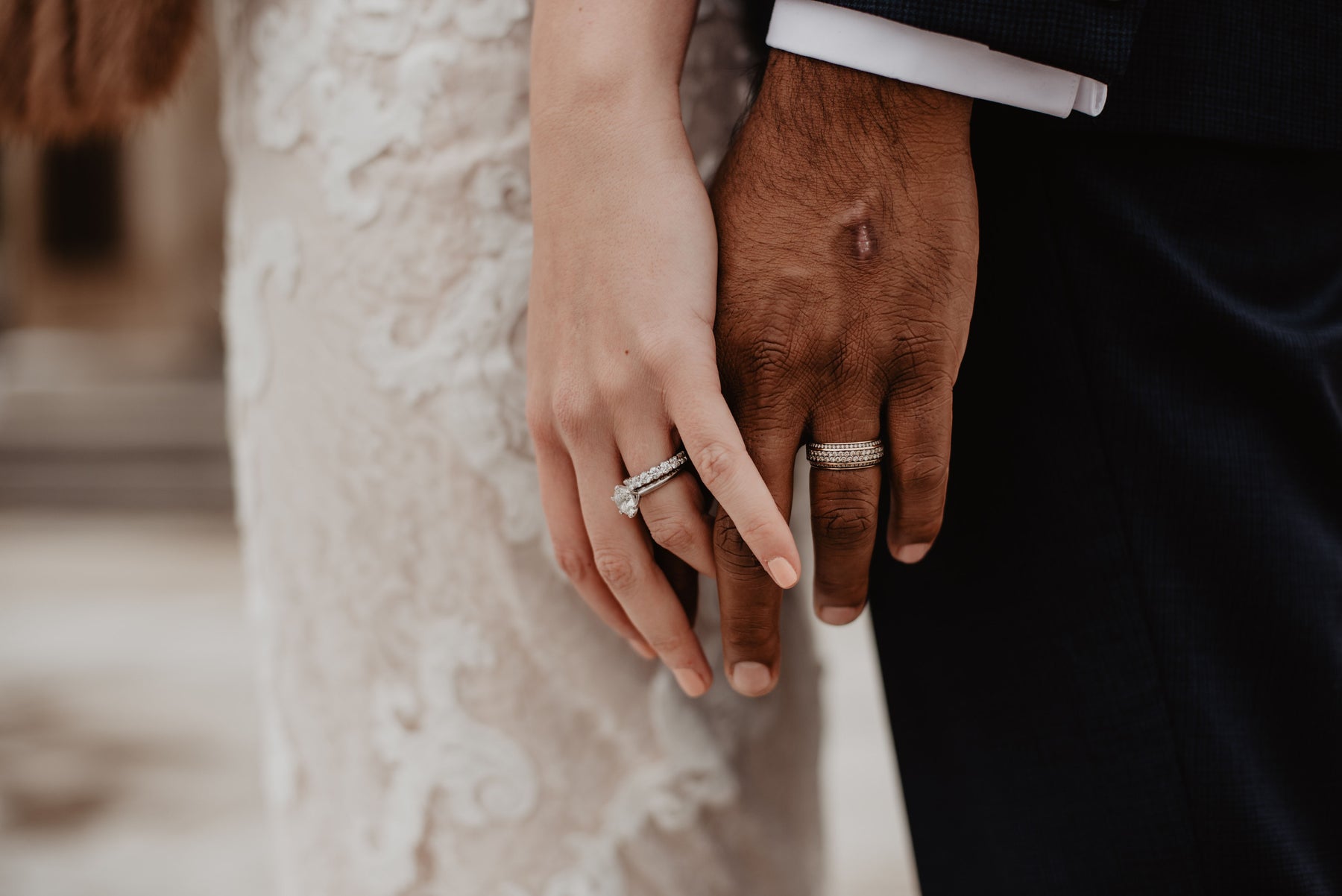 Cose-up photo of a bride and groom holding hands, showcasing their wedding rings. 